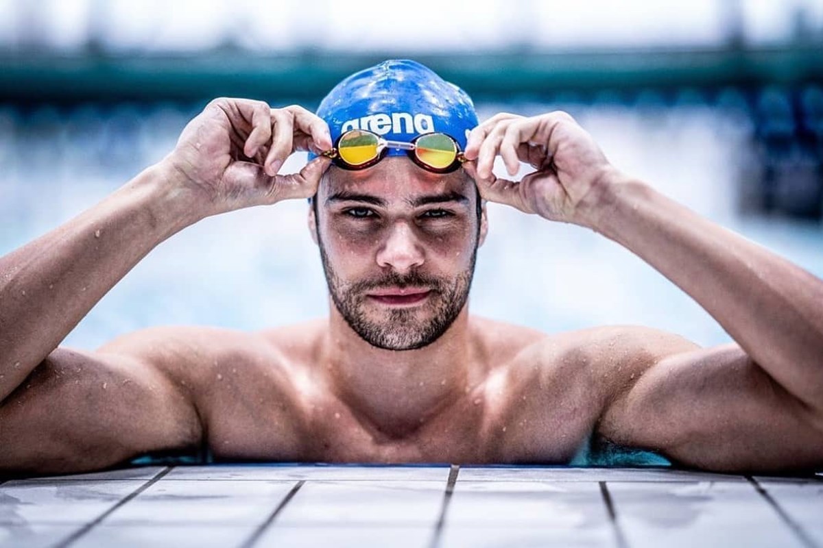 Foto colorida de homem dentro de piscina mexendo em óculos de natação - Metrópoles