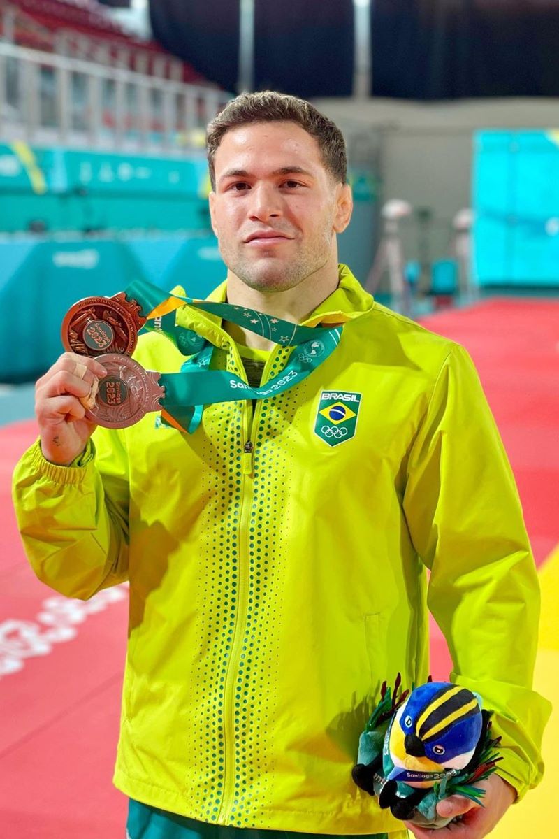 Foto colorida de homem segurando medalhas - Metrópoles