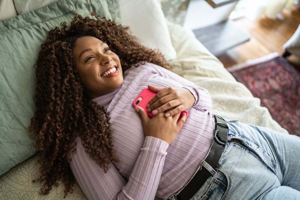 Mulher com o celular deitada na cama 