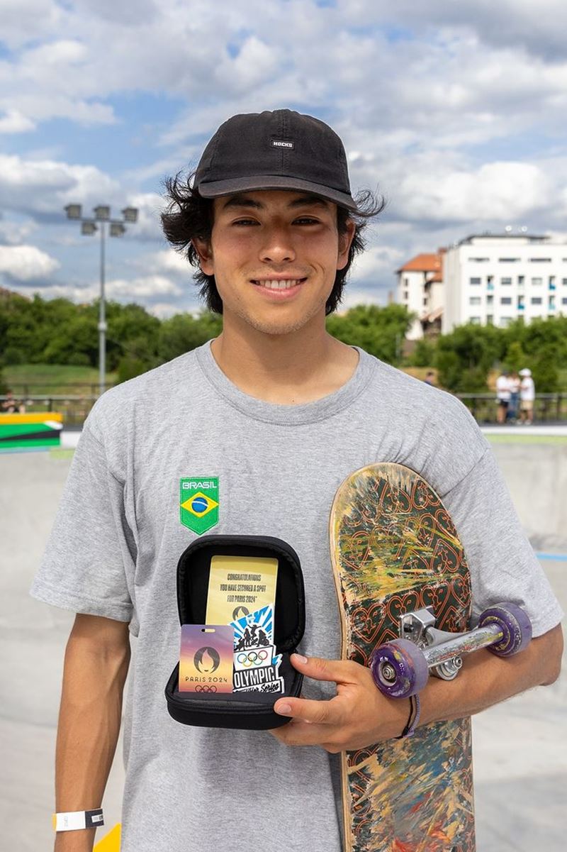 Foto colorida de homem segurando skate e pequenos cartazes - Metrópoles