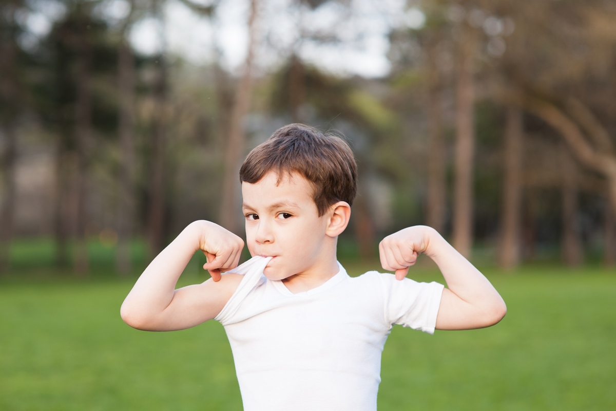 garoto saudável mostra músculos em um fundo de grama - Metrópoles - atividade física para ciranças