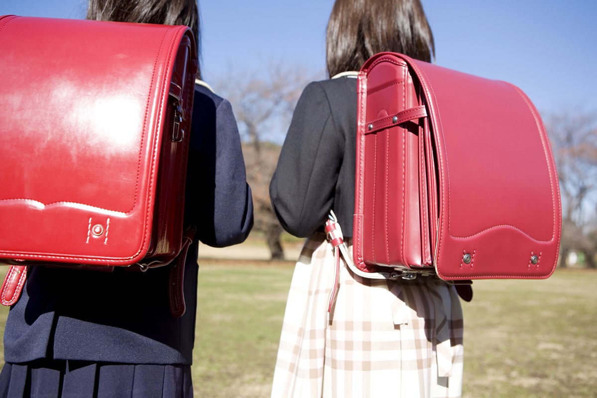 Duas garotas posam de costas expondo suas mochilas vermelhas idênticas