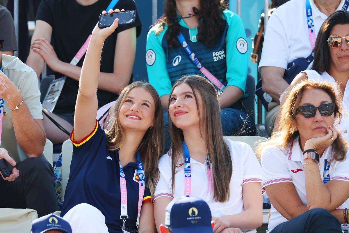 Foto colorida de duas mulheres em uma arquibancada. Elas estão tirando uma selfie - Metrópoles