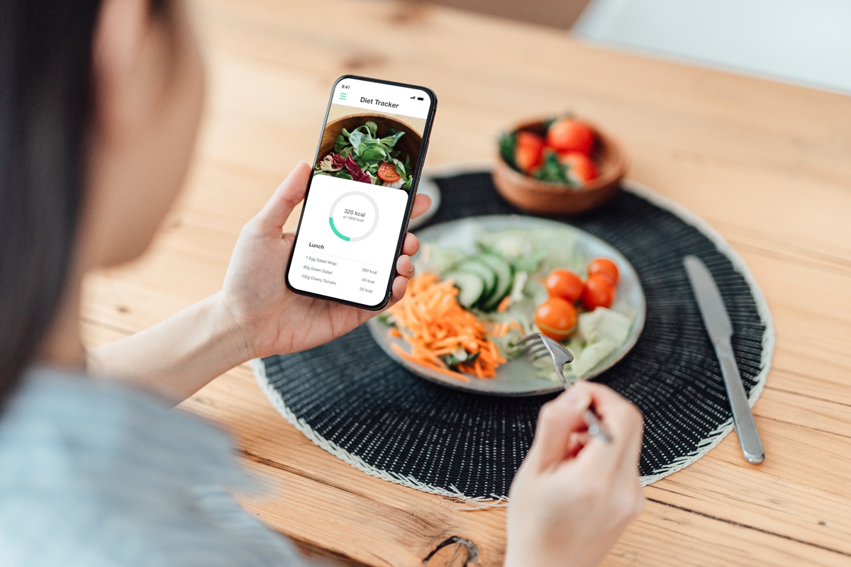 Mão segurando celular e prato de comida saudável logo à frente - Metrópoles