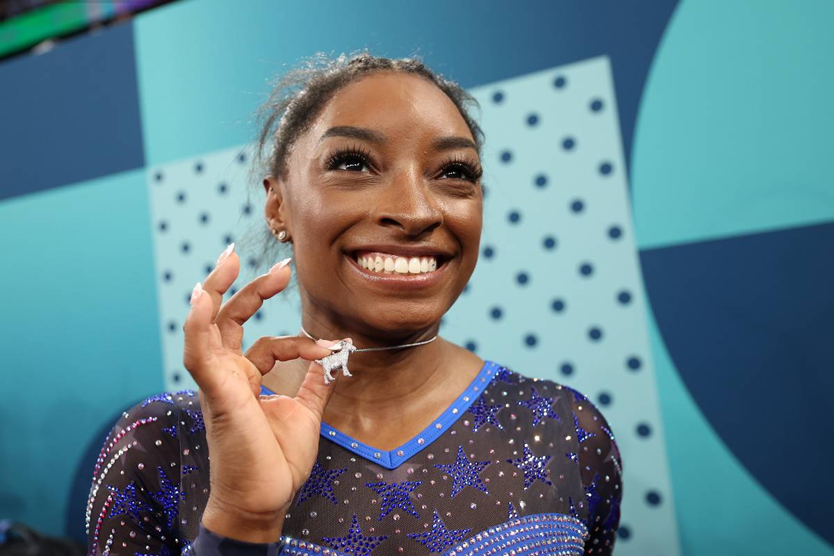 Na imagem colorida, Simone Biles sorri e mostra colar de cabra - Metrópoles