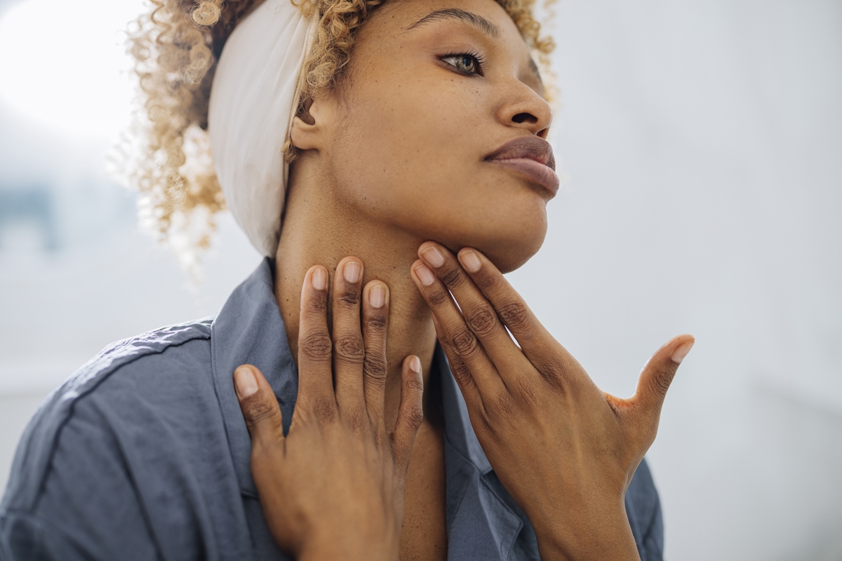 Mulher negra aplicando creme no pescoço com as duas mãos - Metrópoles