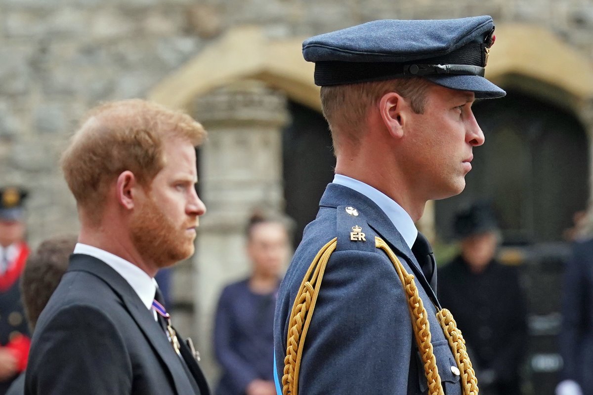 Foto colorida de dois homens em fila. Um usa terno e o outro traje militar britânico - Metrópoles