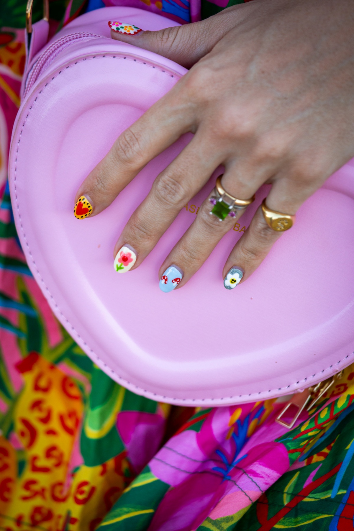 A imagem mostra uma mão com unhas pintadas segurando uma bolsa rosa com formato de coração.