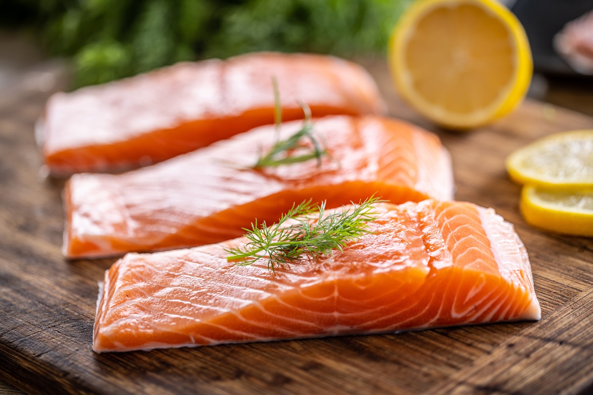 Foto de stock de Filetes de salmão cru em tábua de madeira com endro, alecrim e limão.