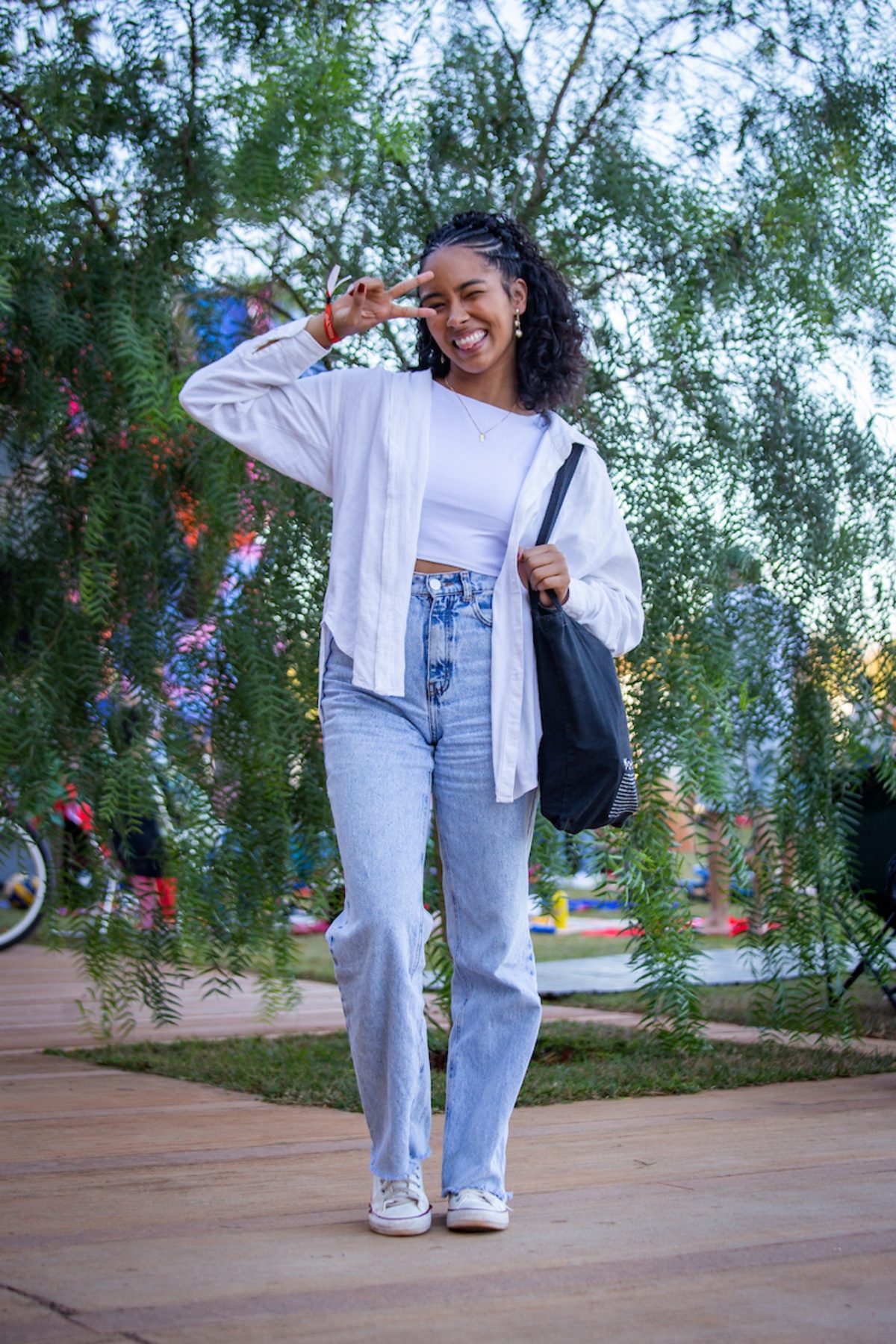 Menina posa para a foto. Com uma camiseta e camisa branca, ela combina seu visual com uma calça jeans azul e uma bolsa preta