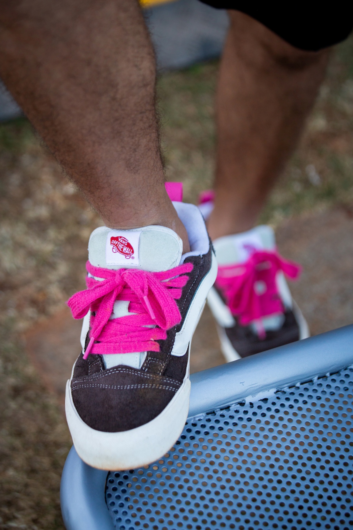 A imagem mostra um tênis apoiado sob um banco. Exibindo um cadarço rosa, o calçado vem com as cores preto e branco