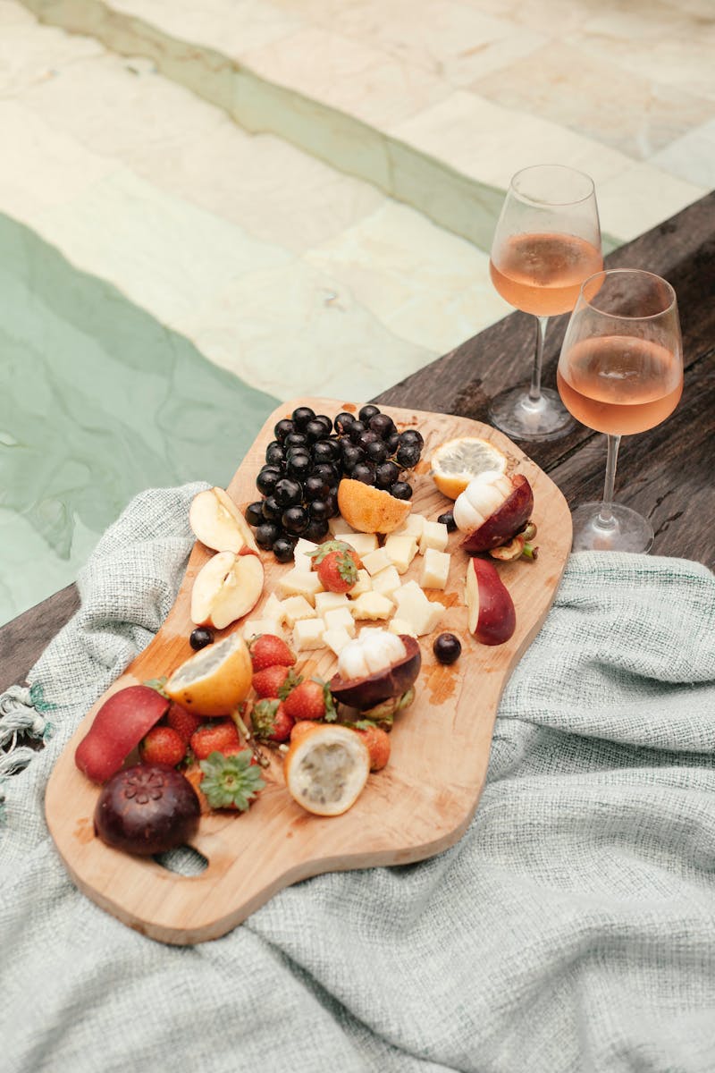 Tábua de madeira com frios ao lado de taças de vinhos rosé próxima à piscina - Metrópoles