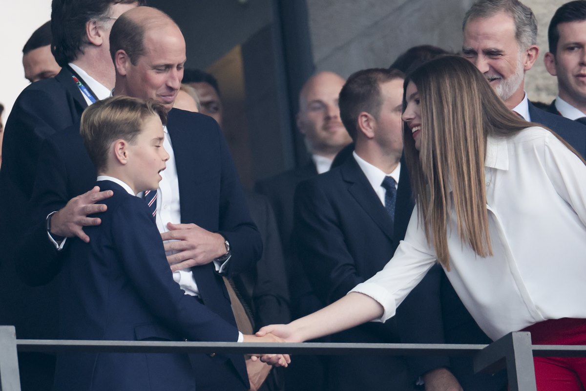 Foto colorida de menino cumprimentando mulher. Um homem está com a mão no ombro do garoto - Metrópoles