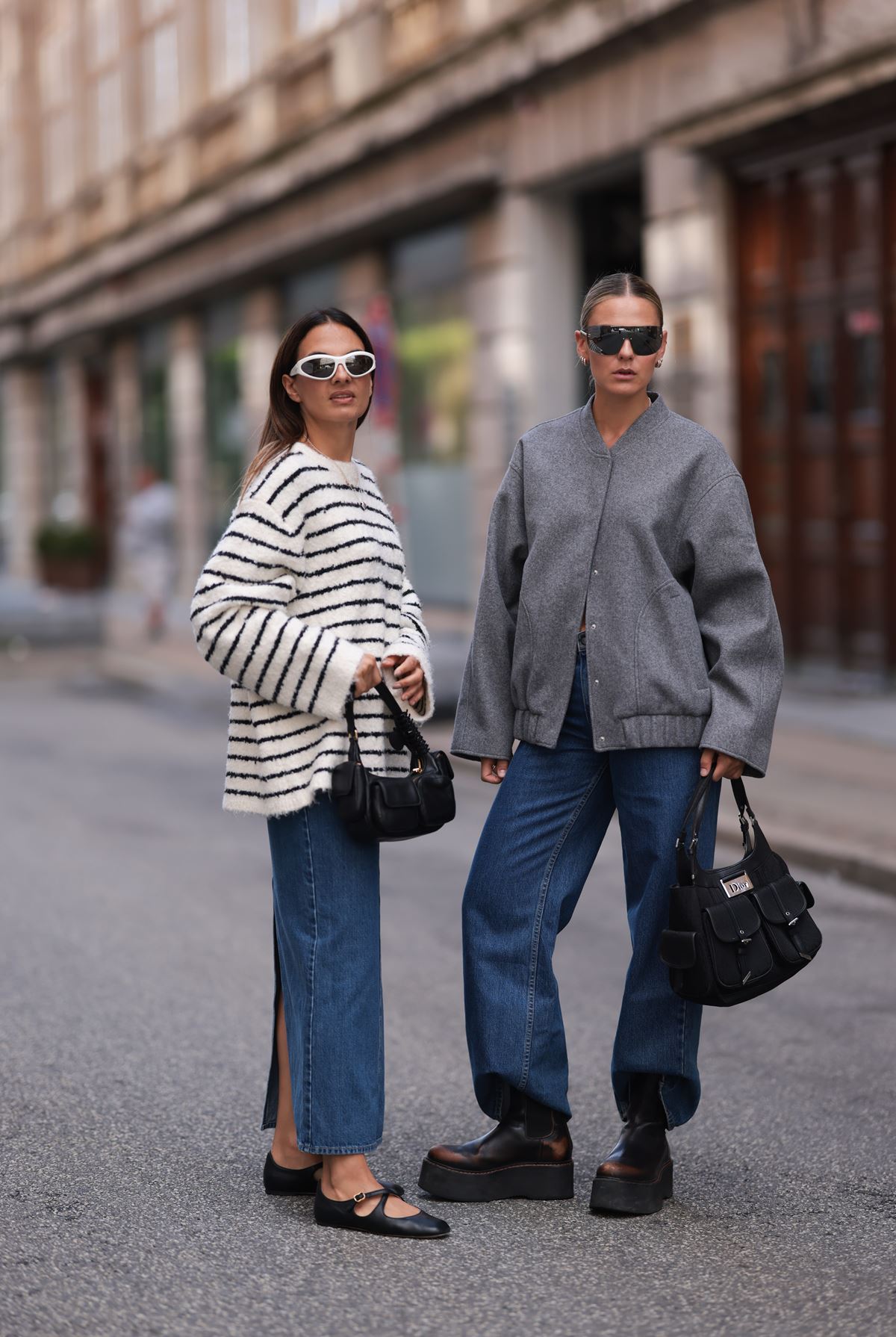 Na rua, em Copenhague, duas mulheres andam usando óculos escuros. Uma usa saia jeans com blusa listrada, enquanto a outra está com calça jeans e jaqueta cinza - Metrópoles