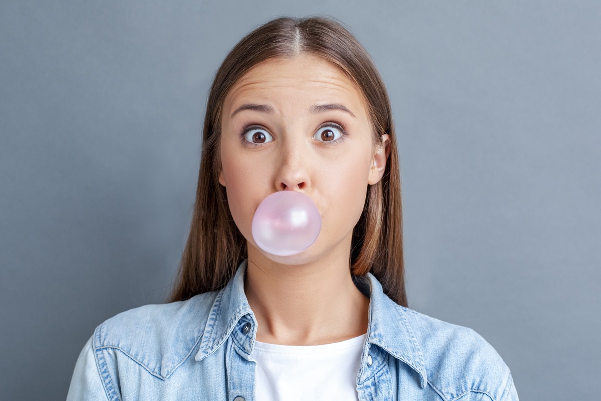 Foto colorida de mulher fazendo bola com chiclete - Metrópoles