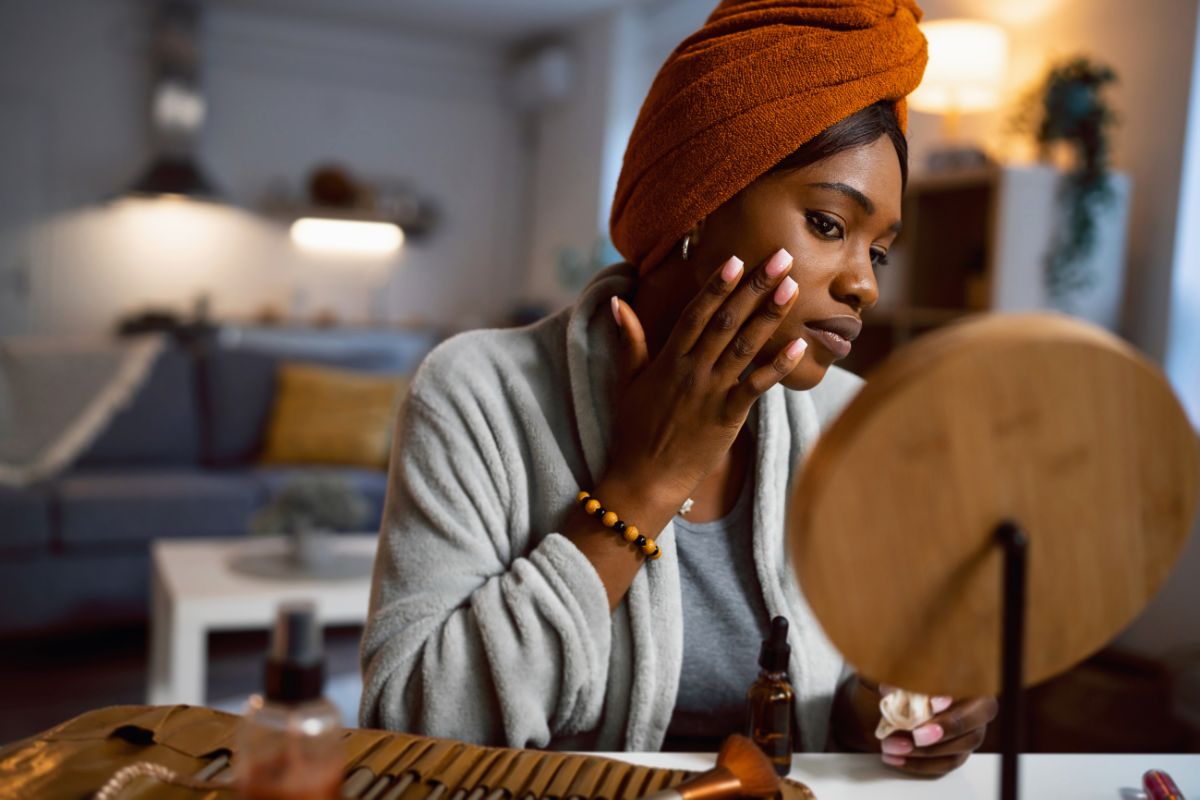 Foto colorida de uma mulher negra fazendo skincare - Metrópoles