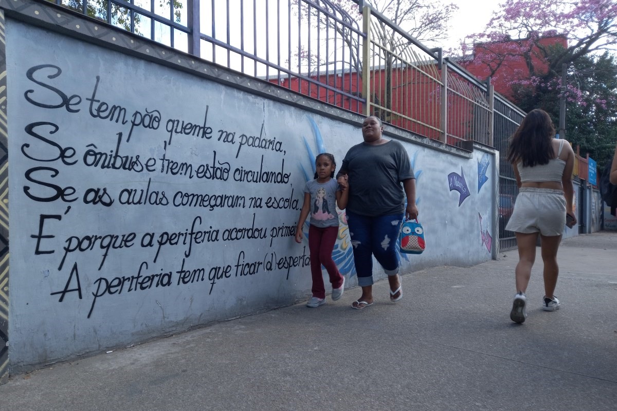 Imagem mostra mulher e criança caminhando em frente a muro - Metrópoles