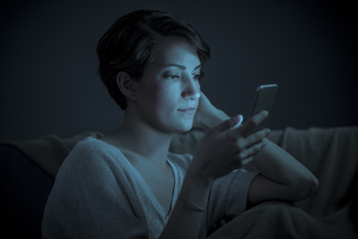 Imagem mostra uma mulher no escuro, iluminada pela luz azul do celular - Metrópoles