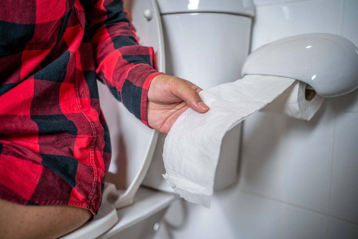 Foto colorida de mulher puxando o papel higiênico enquanto está sentada no vaso sanitário - Metrópoles