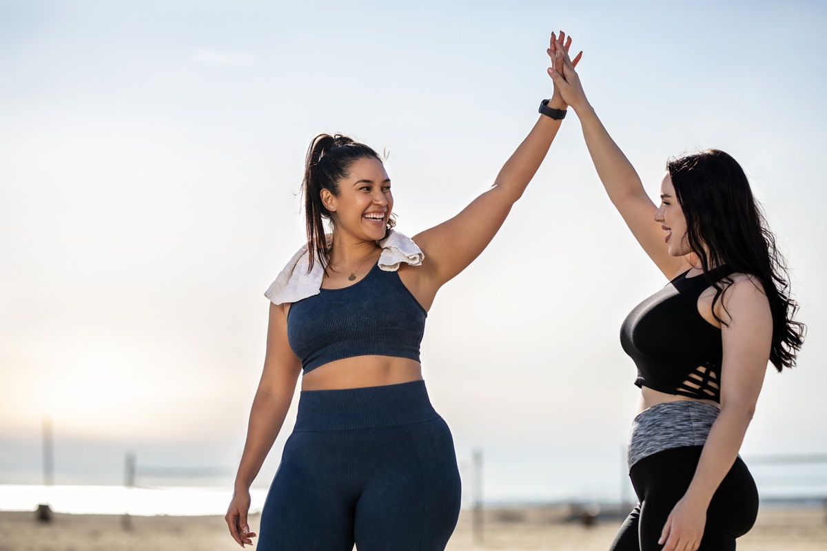 Foto colorida de mulheres se cumprimentando. Elas usam roupa de academia - Metrópoles