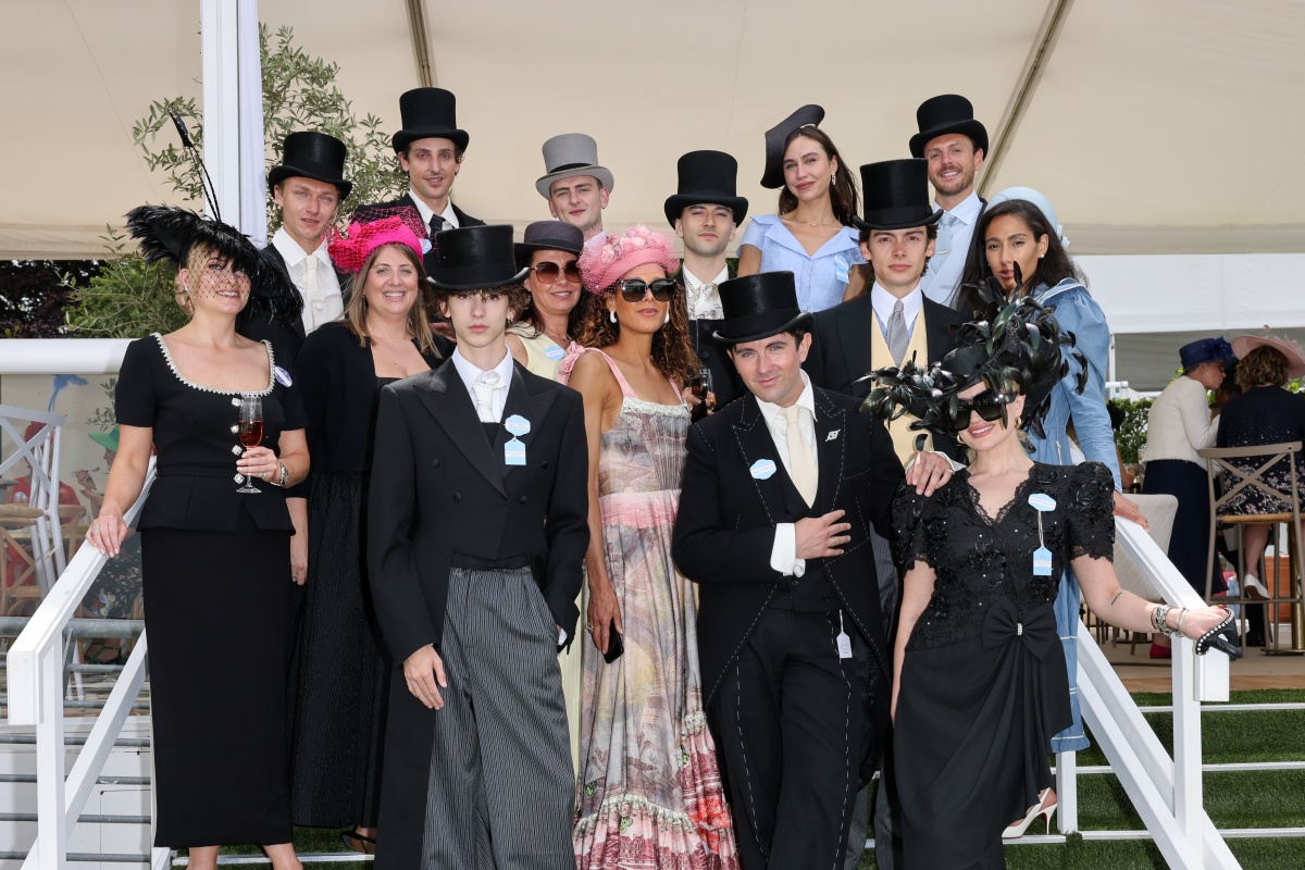 Grupo de pessoas posa para a foto. Em evento social, homens e mulheres aparecem com chapéus variados e trajes de gala.