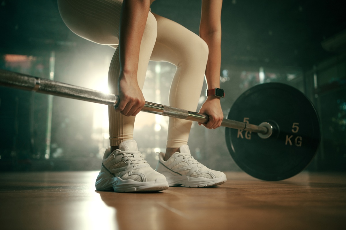 Jovem fazendo levantamento terra com barra pesada no ginásio, atleta feminina forte com corpo musculoso levantando pesos, exercitando com barra - Metrópoles