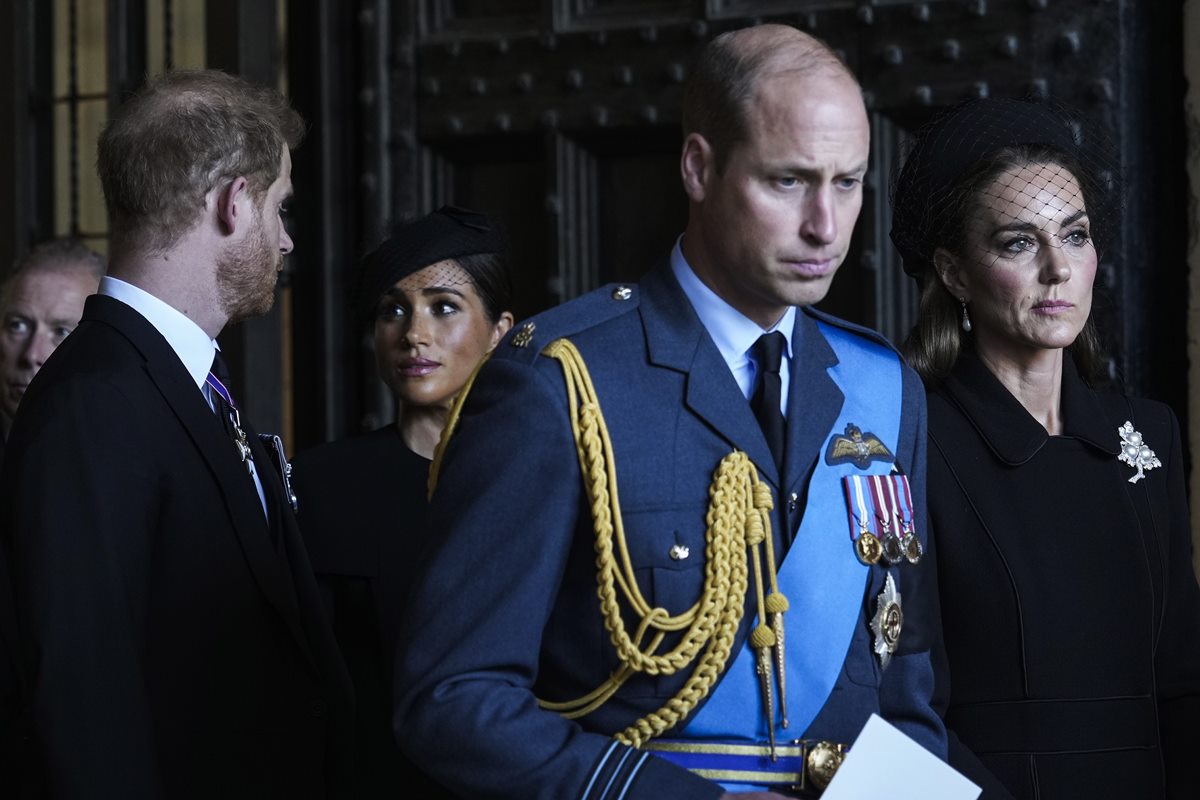 Foto colorida de um homem com traje militar britânico ao redor de duas mulheres com roupas pretas e um homem com roupa preta - Metrópoles