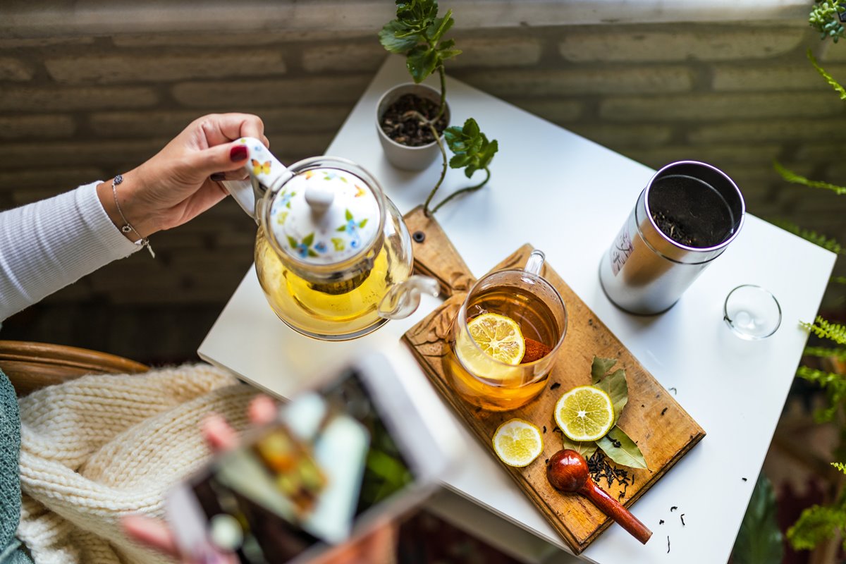 Foto colorida de mesa com frutas secas, chá, xícaras e mão feminina segurando um bule - Metrópoles