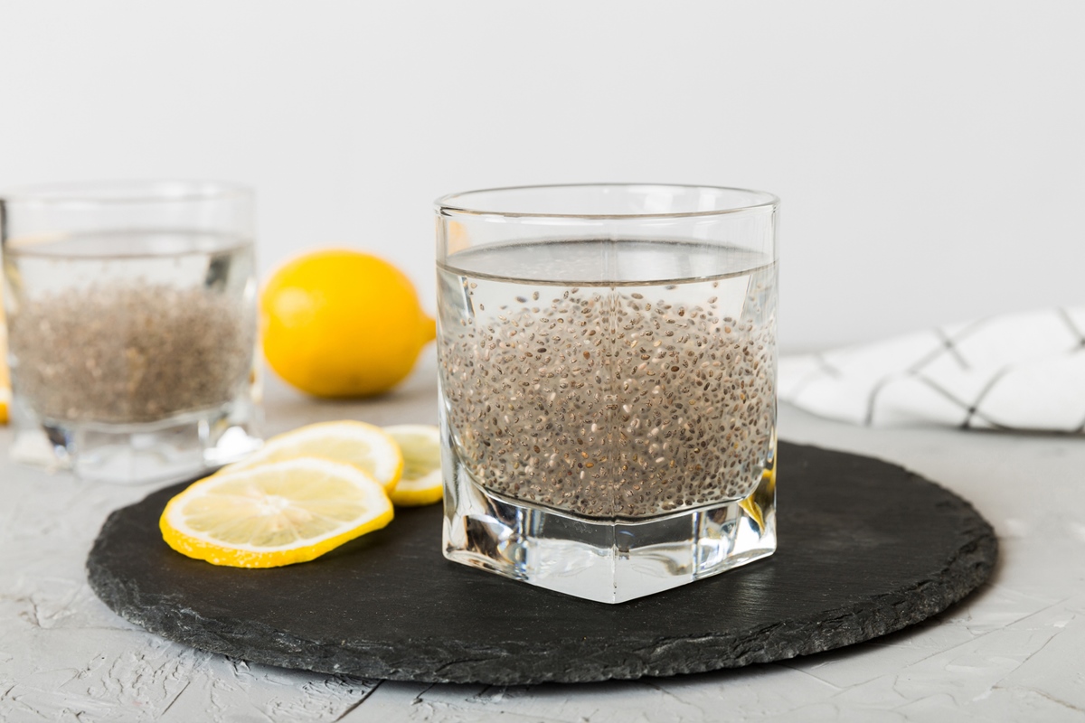 Copo com água e sementes de chia e limão no fundo da mesa,