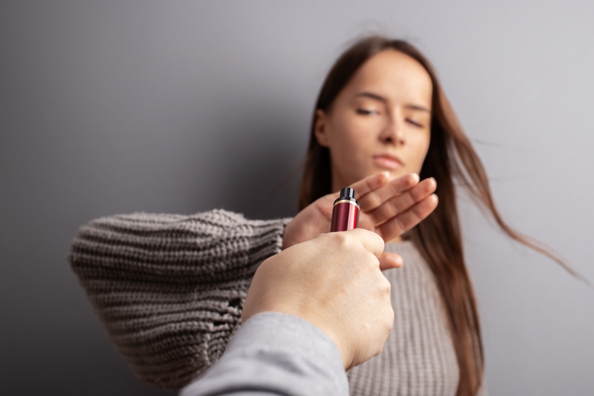 Foto colorida de mão masculina segurando vape e mulher afastando o cigarro eletrônico - Metrópoles