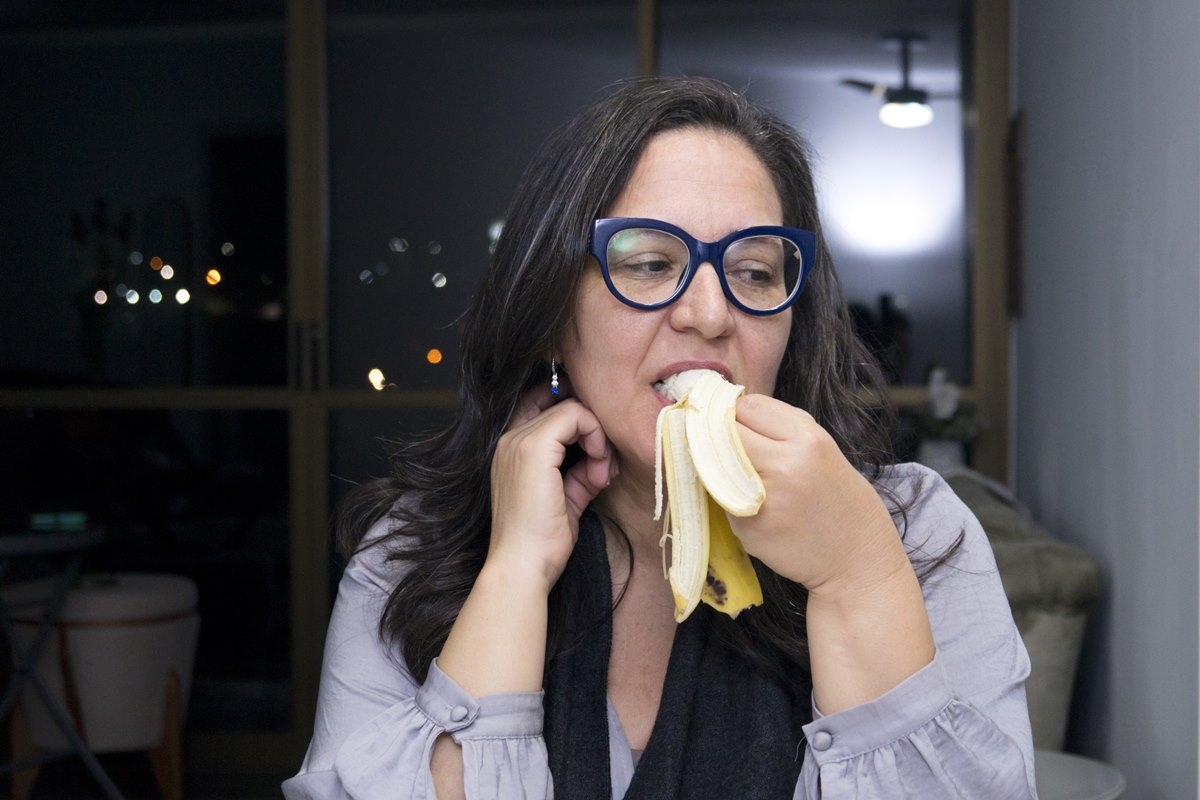 Foto colorida de mulher comendo banana à noite - Metrópoles