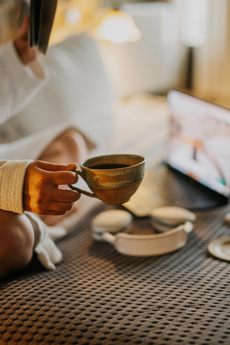 Mão segurando xícara de café com objetos ao fundo - Metrópoles