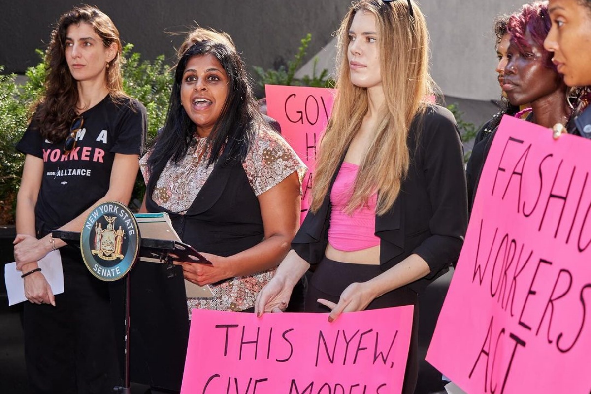 Modelos protestam na cidade de Nova York com cartazes rosa com suas reinvidicações escritas em preto.