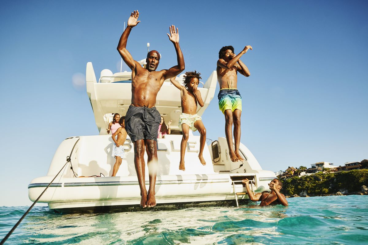 Foto de homens e dois garotos pulando de um barco para o mar - Metrópoles