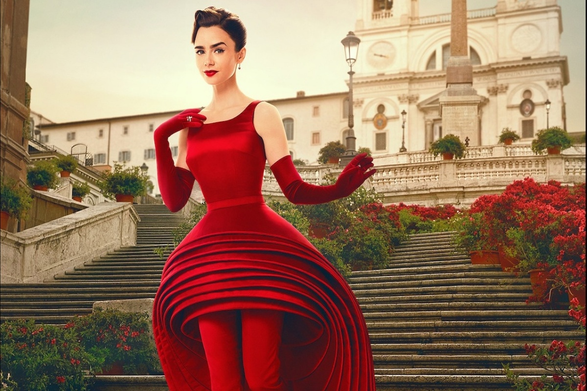 A imagem mostra uma moça descendo uma escadaria. Com um vestido vermelho, a moça usa acompanhamentos no visual que seguem a mesma cor do vestido