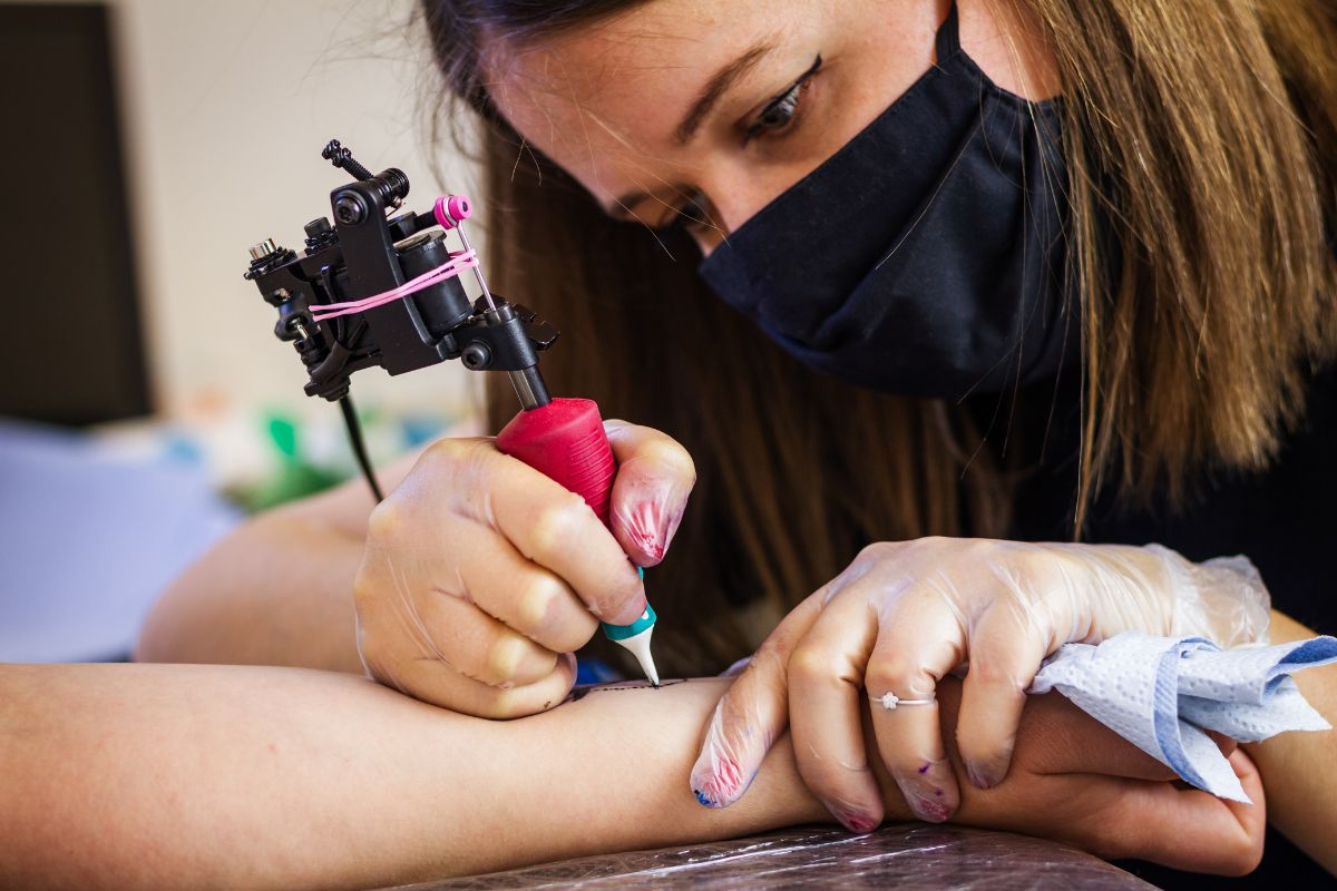 Foto colorida de uma mulher tatuando - Metrópoles