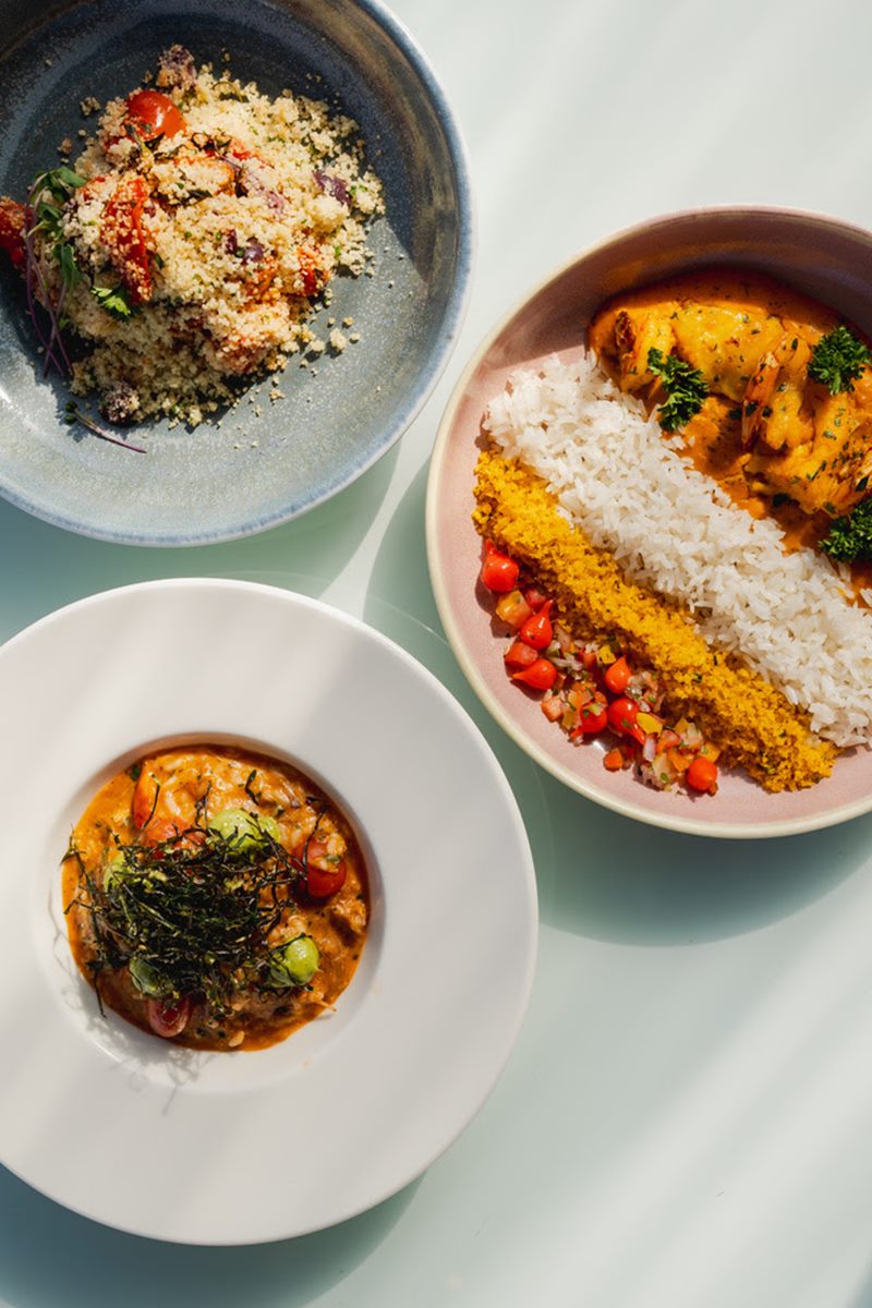 Na imagem colorida, um menu de comida em três pratos dispostos em cima de uma mesa branca - Metrópoles 