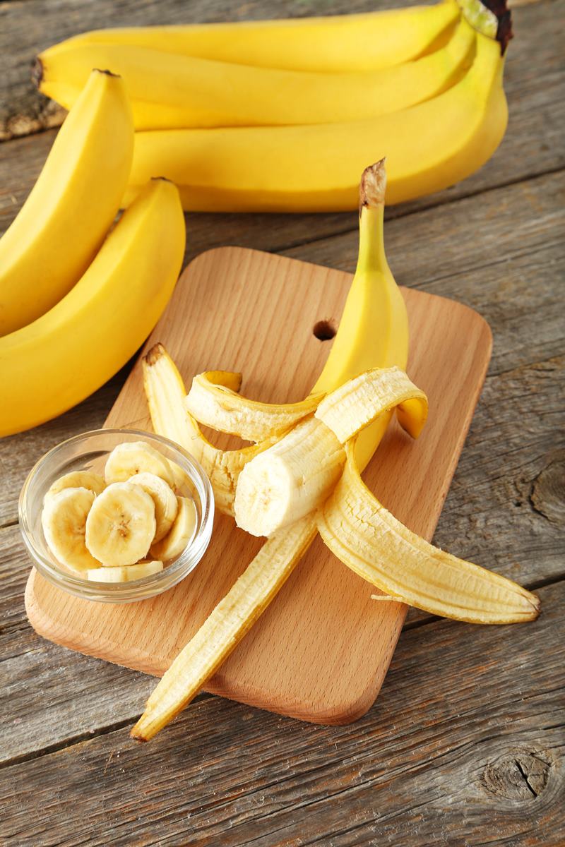 Foto colorida de pencas de bananas, uma fruta descascada e outra cortada dentro de uma tigela de vidro - Metrópoles