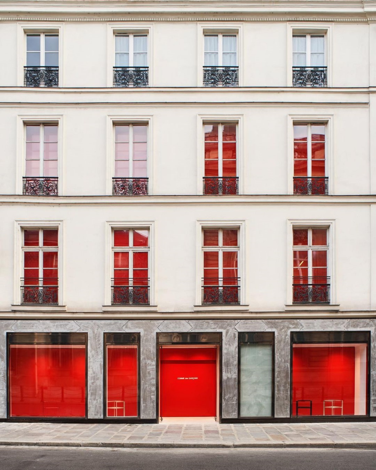 A imagem mostra um prédio branco de quatro andares com o interior vermelho