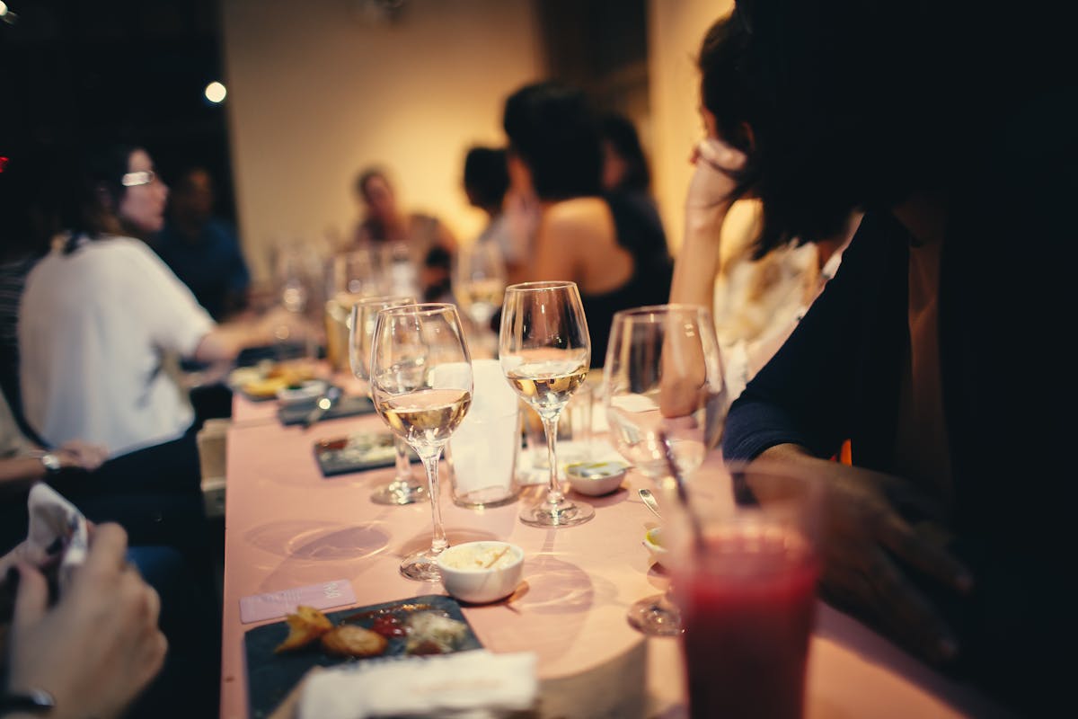 Mesa com várias taças e pratos de happy hour e pessoas ao fundo - Metrópoles