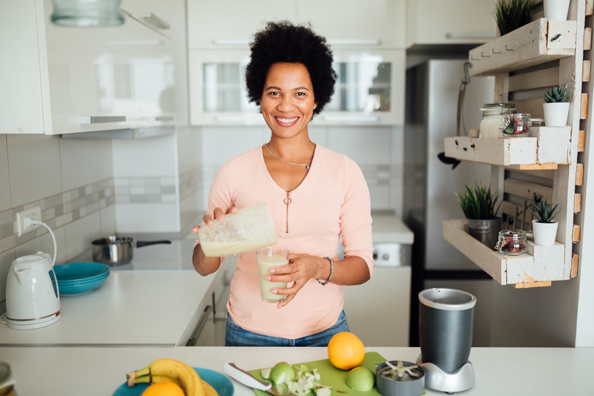 Foto colorida de mulher tomando vitamina. Ela está em uma cozinha - Metrópoles