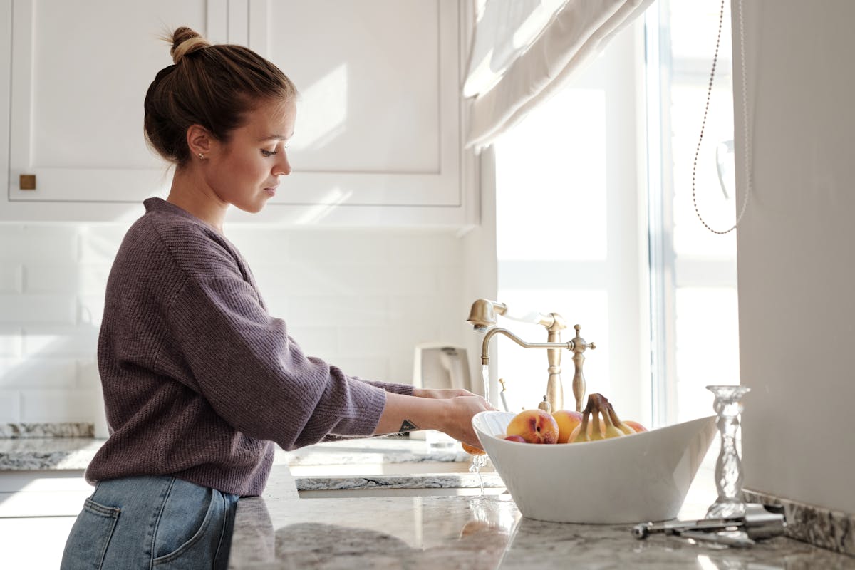 Jovem mulher lavando alimentos em pia de cozinha - Metrópoles