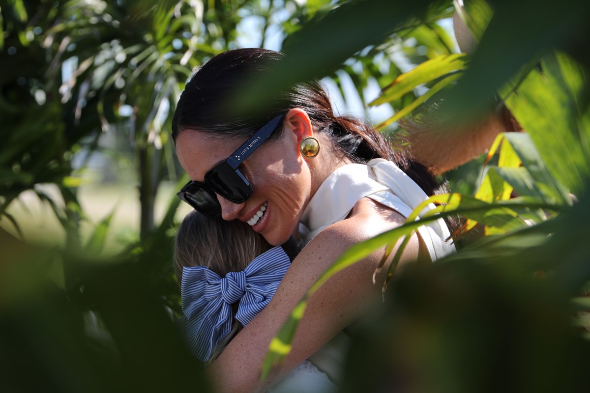 Foto colorida de mulher abraçando menina em jardim - Metrópoles