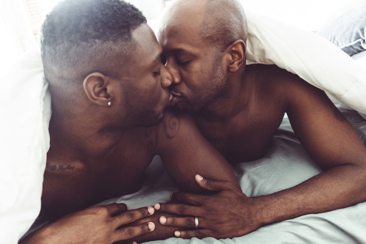 foto colorida de dois homens se beijando na cama 