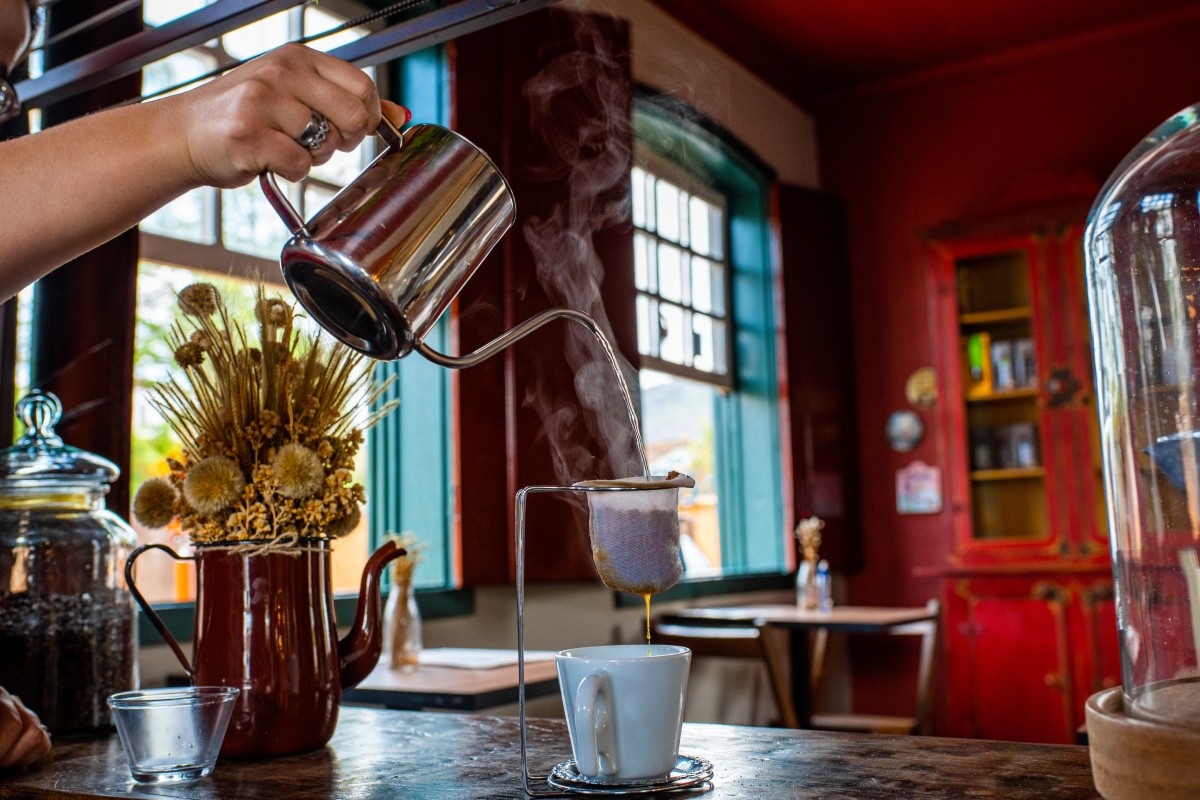 Fotografia colorida mostrando mão segurando bulê de café e colocando em xícara-Metrópoles