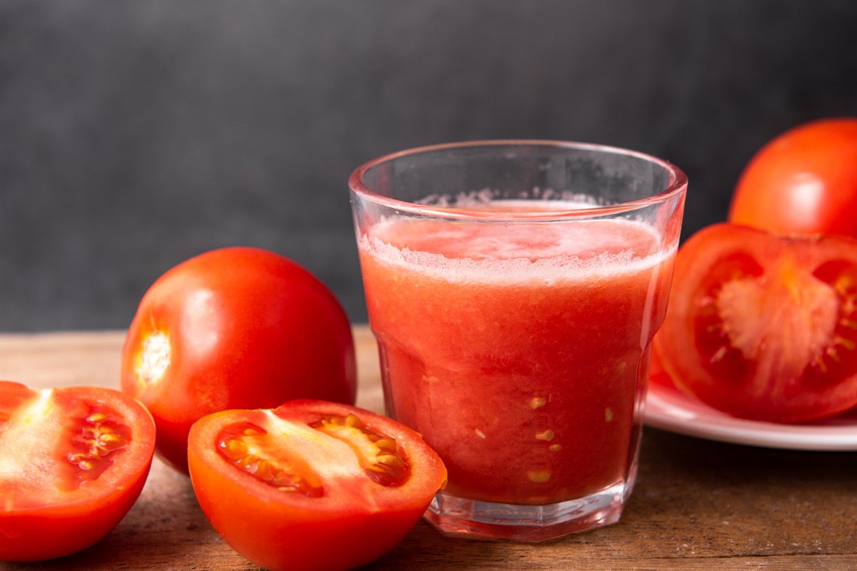 Foto colorida de copo com suco de tomate. Ao lado, tem tomates inteiros e cortados - Metrópoles