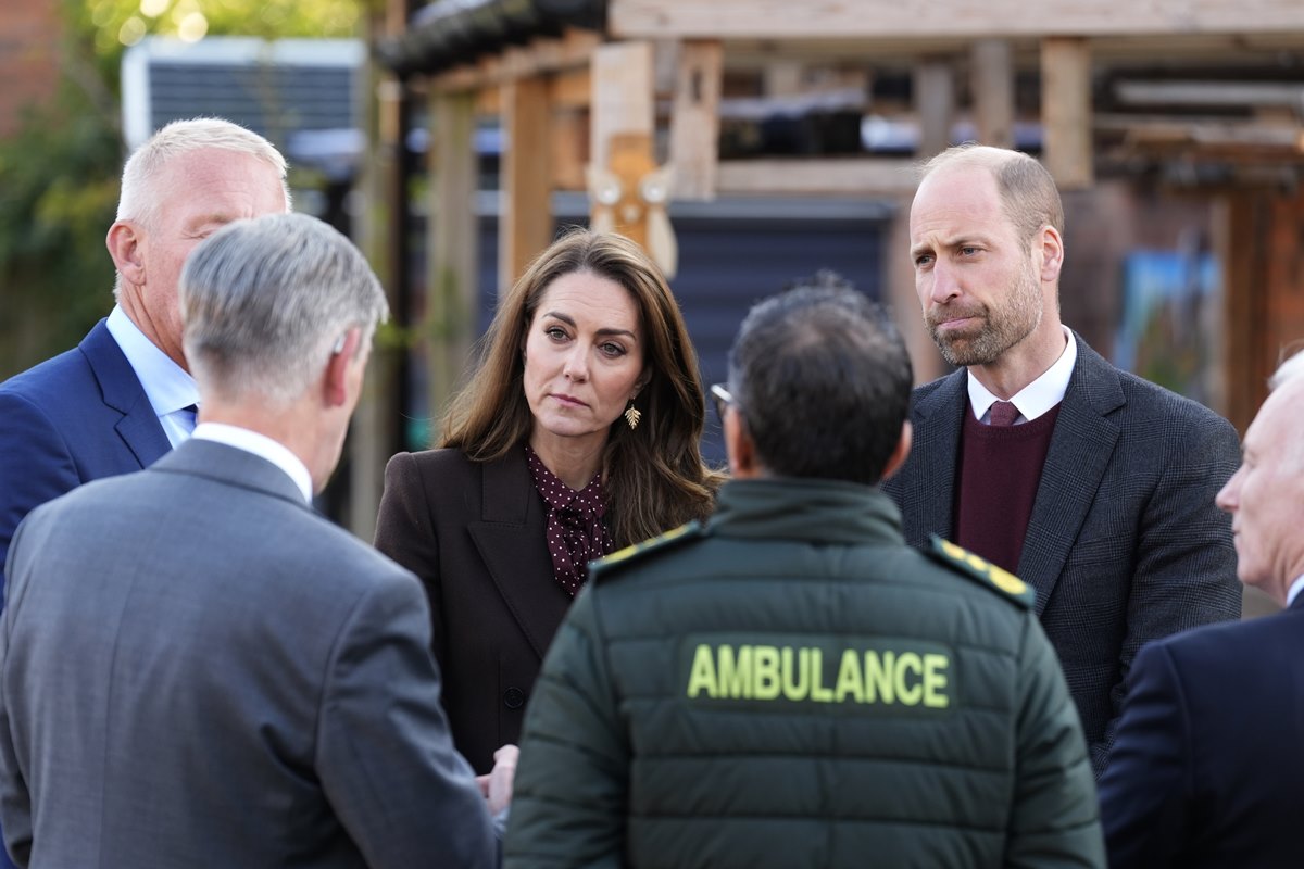 Foto colorida de mulher e homem conversando com grupo masculino. Um dos homens está com um colete escrito ambulance - Metrópoles