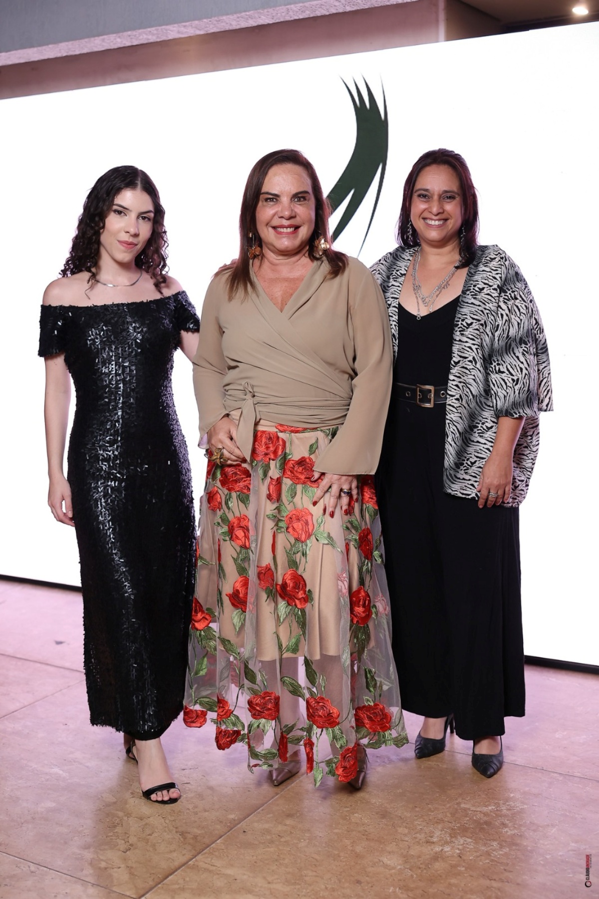 A imagem mostra três mulheres posando para a foto. Olhando diretamente para a câmera, todas sorriem enquanto são fotografadas