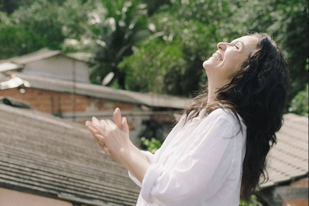 foto colorida de mulher de blusa branca olhando para cima e sorrindo - metrópoles