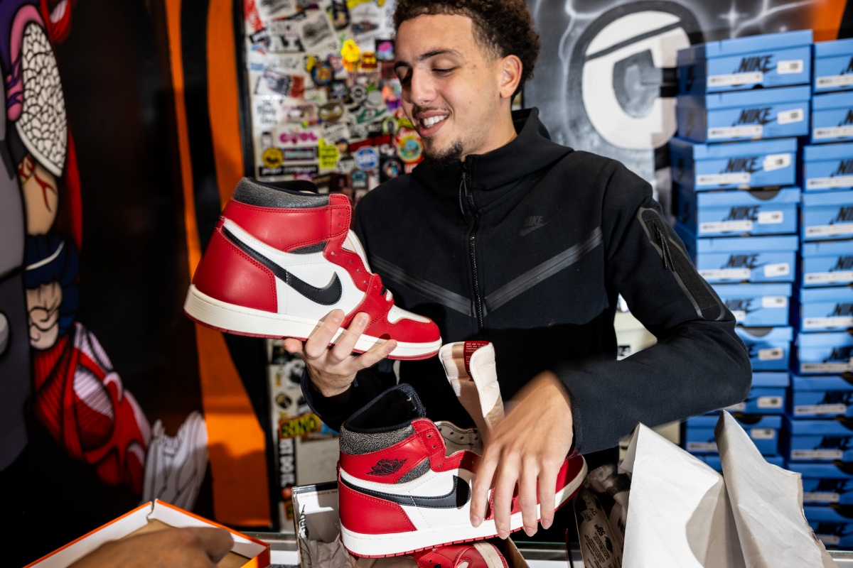 A imagem mostra um jovem segurando um par de Jordans 1 nas cores branco, vermelho e preto